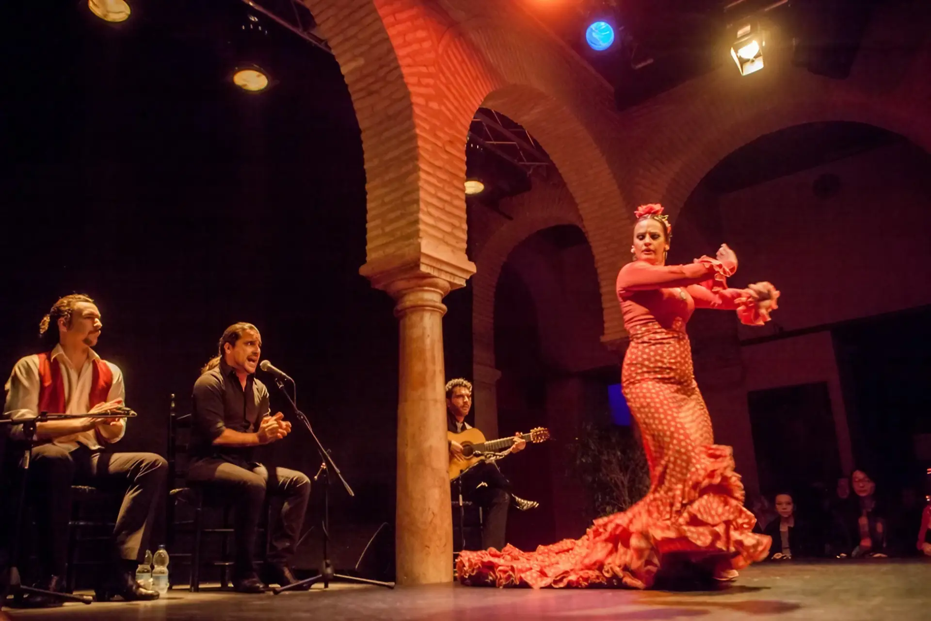 Flamenco dancer in red and white spotted dress with singers and guitarists performing at the Museum of Flamenco in Seville. The Bienal de Flamenco is being held in Seville in 2026 - andalucia.org - © TURISMO ANDALUZ