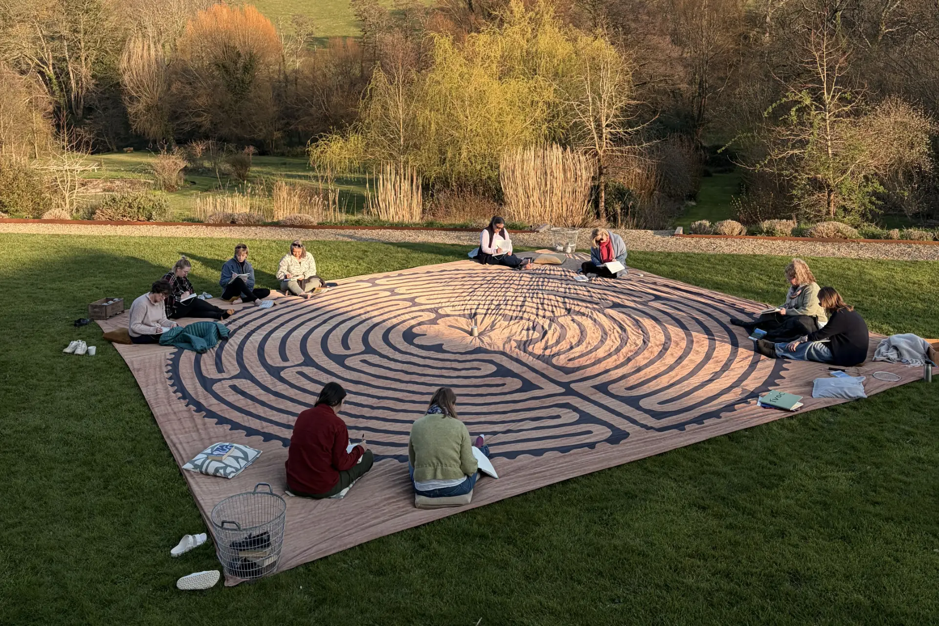 Group of women seated around a large labyrinth-patterned mat during an outdoor writing retreat in landscaped gardens