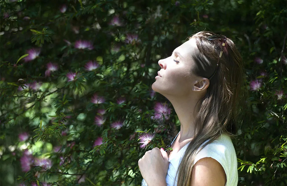 Woman relaxing with sun on her face outdoors by flowers. Credit: Photo by Oleksandr P: https://www.pexels.com/photo/woman-closing-her-eyes-against-sun-light-standing-near-purple-petaled-flower-plant-321576/