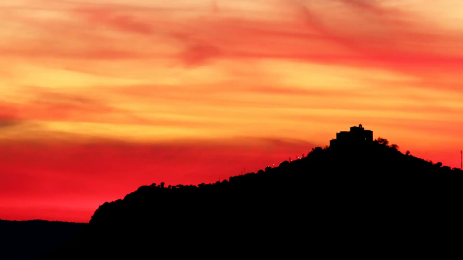 sunset over Sierra Morena with building on ridge and trees in silhouette against a red and orange sky